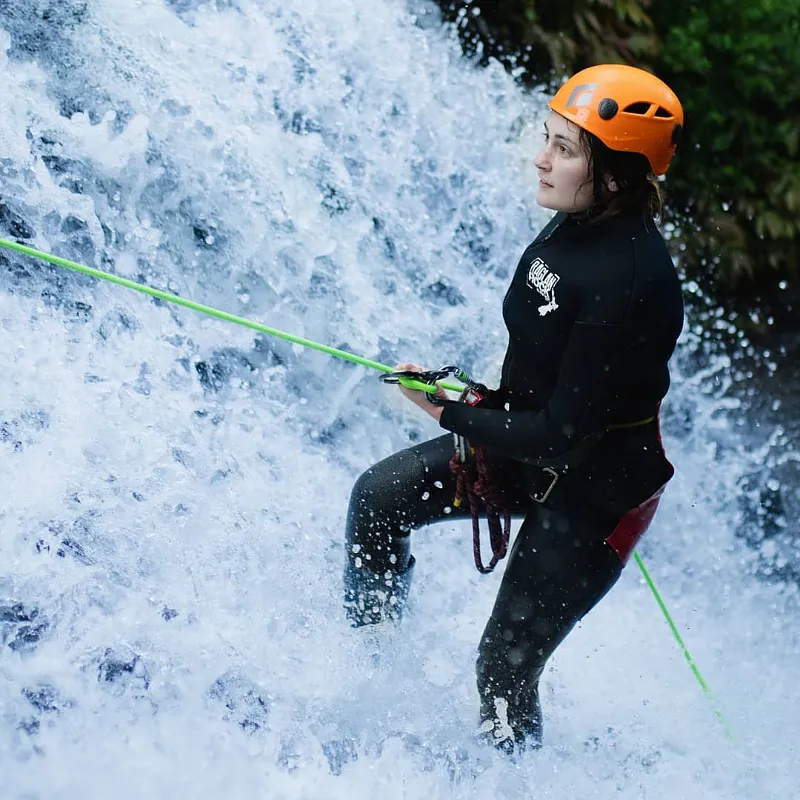 Canyoner in an orange helmet abseiling beside a rushing waterfall