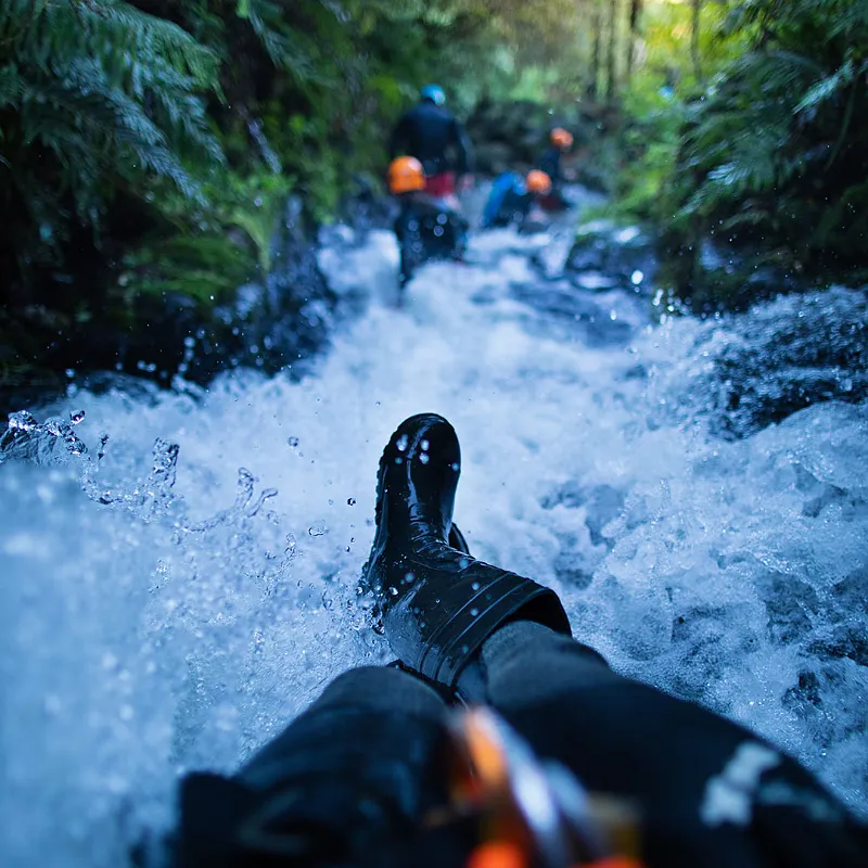 Canyoner sliding feet-first down whitewater in the Karioi canyon