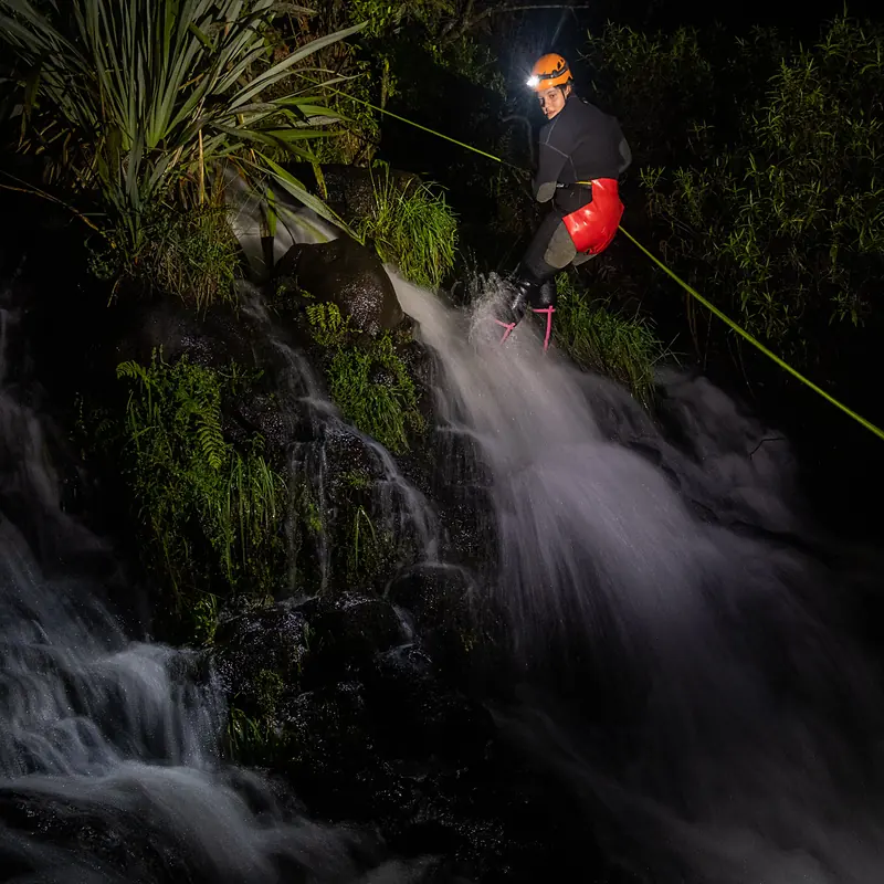 Canyoner abseiling down a waterfall at night with a headlamp