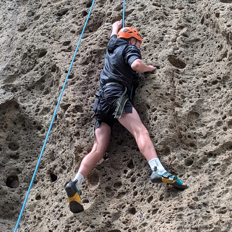Climber bridging on pocketed rock during a sport climbing course