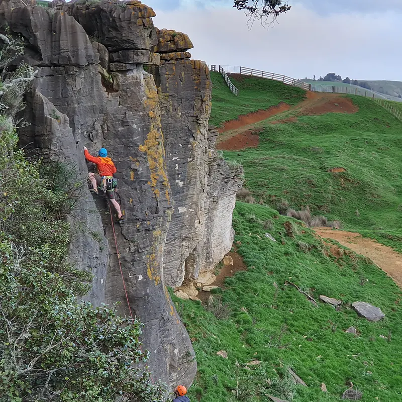 Trad climbing a lichen-covered crag above green farmland