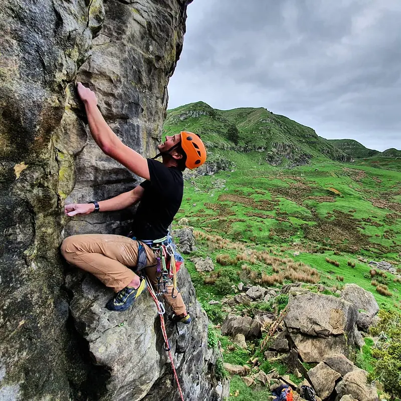 Climber placing trad gear with green hills behind