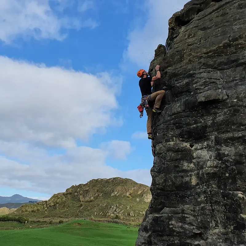 Trad climber on a rock tower against blue sky and farmland